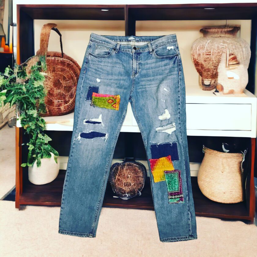 A pair of jeans with colorful patches hanging on a shelf.
