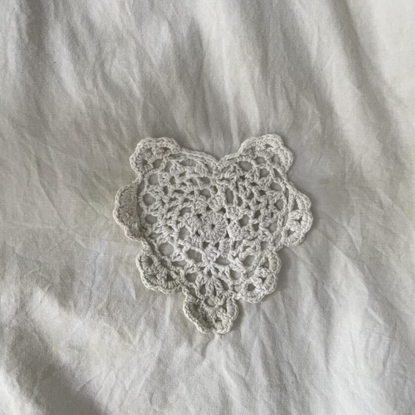 A white crocheted heart on a white bed.