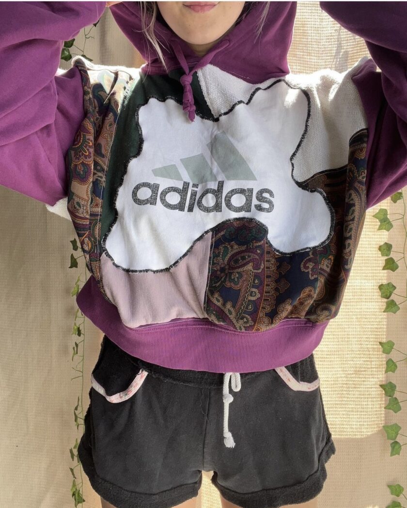 A woman wearing a purple adidas hoodie and shorts.