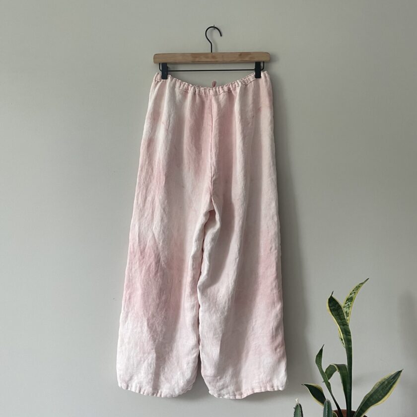 A pair of pink linen pants hanging on a wall.