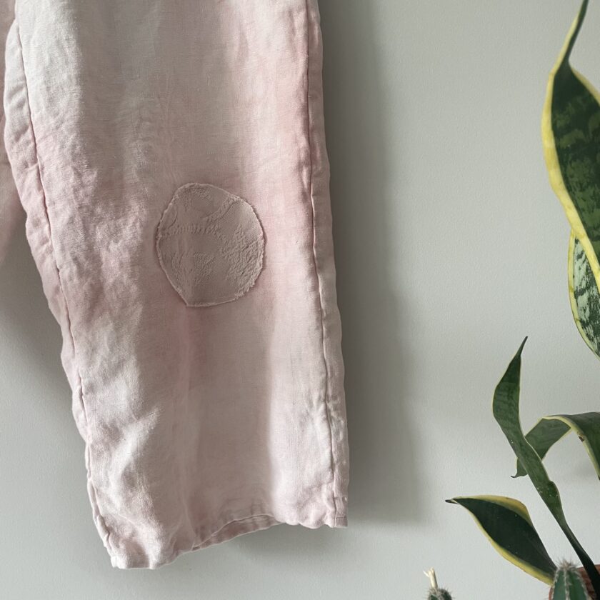 A pair of pink linen pants hanging on a wall.