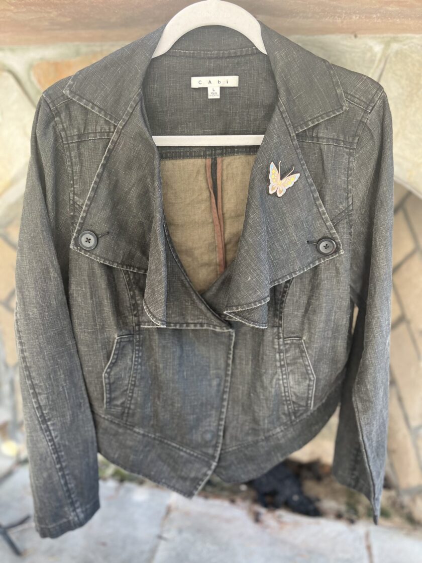 A denim jacket hanging on a hanger in front of a fireplace.