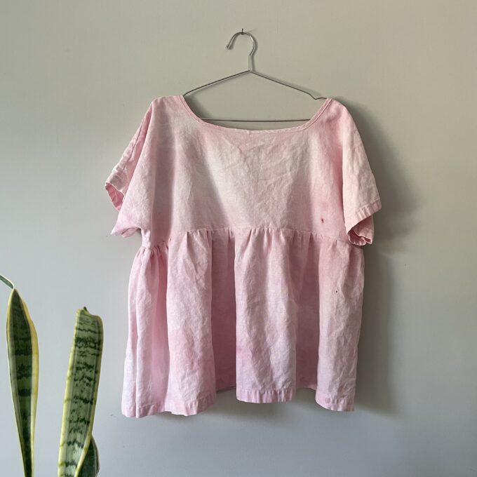 A pink tie dye top hanging on a wall.