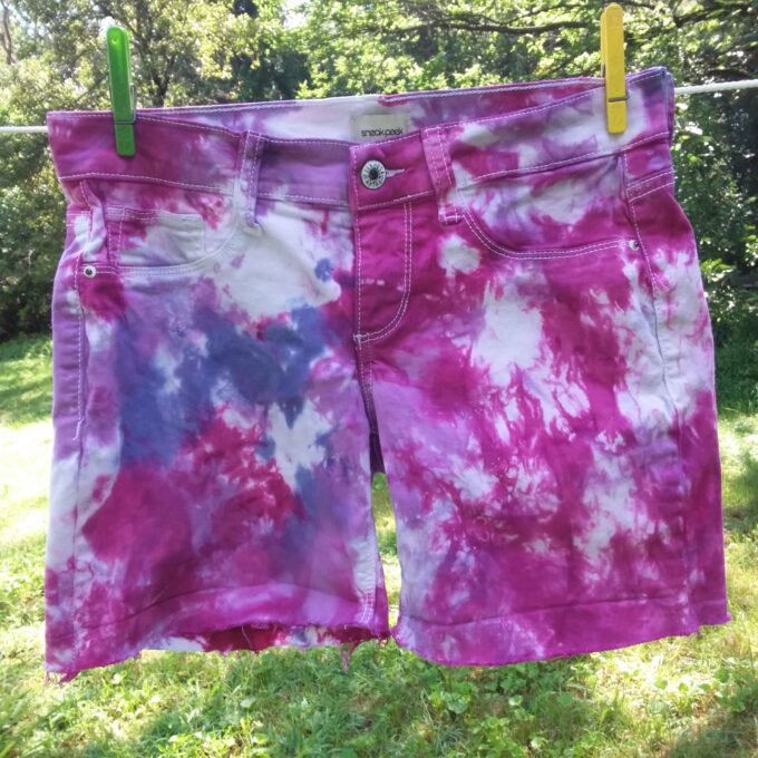 A pair of pink and purple tie dye shorts hanging on a clothes line.