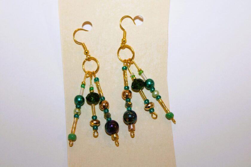 A pair of gold dangling earrings with green and black beads.