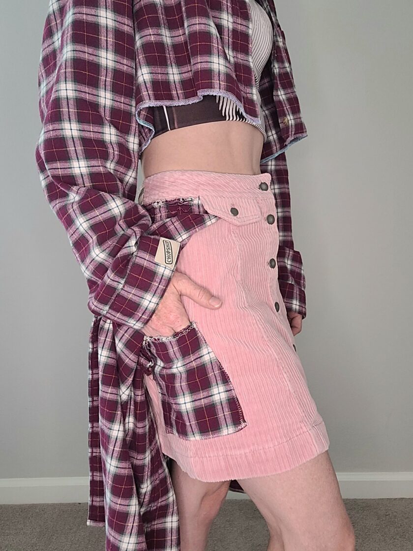 A woman wearing a plaid shirt and pink corduroy skirt.