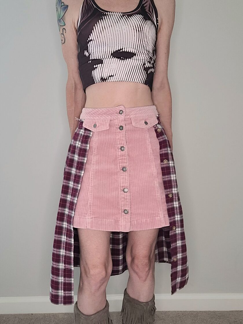 A woman wearing a pink corduroy skirt and a plaid top.