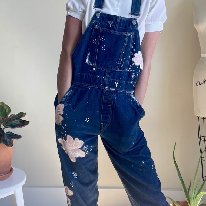 A woman in overalls with flowers painted on them.