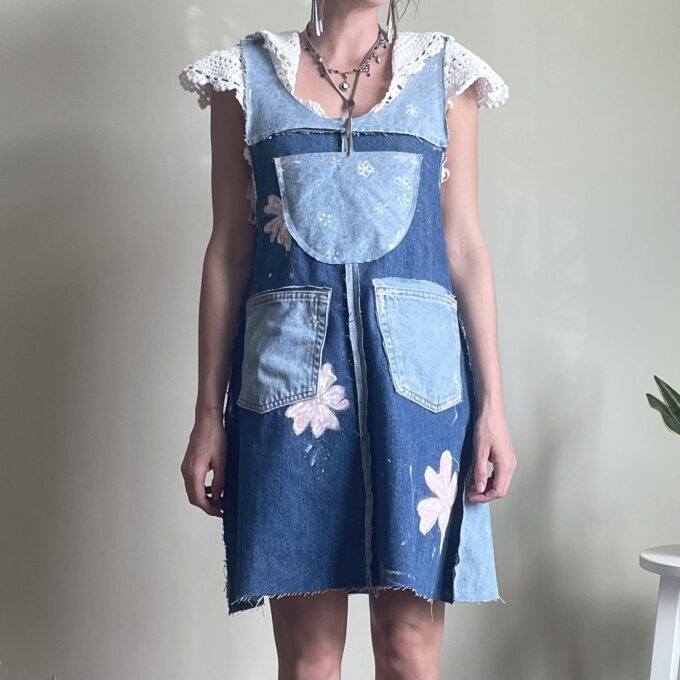 A woman is standing in a room wearing a denim overall dress.