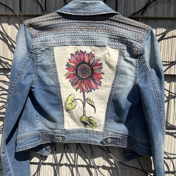 A denim jacket with a sunflower on it.