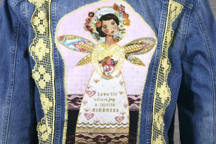 The back of a denim jacket with an angel on it.
