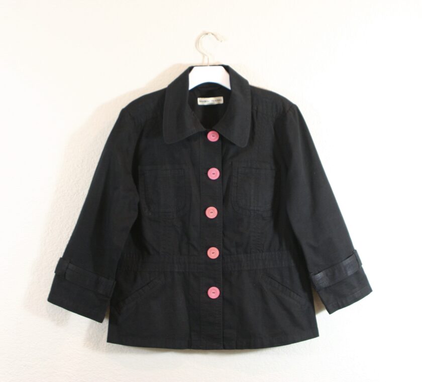A black jacket with pink buttons hanging on a hanger.