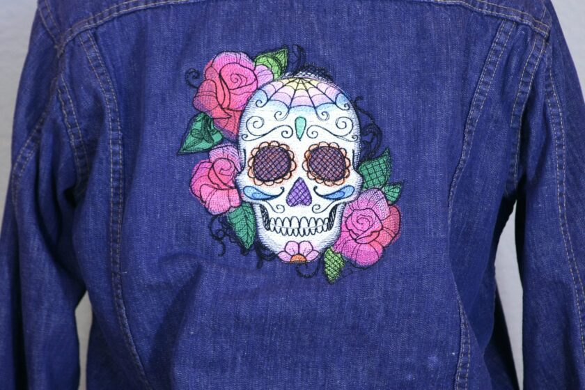 A denim jacket with a sugar skull and roses embroidered on it.