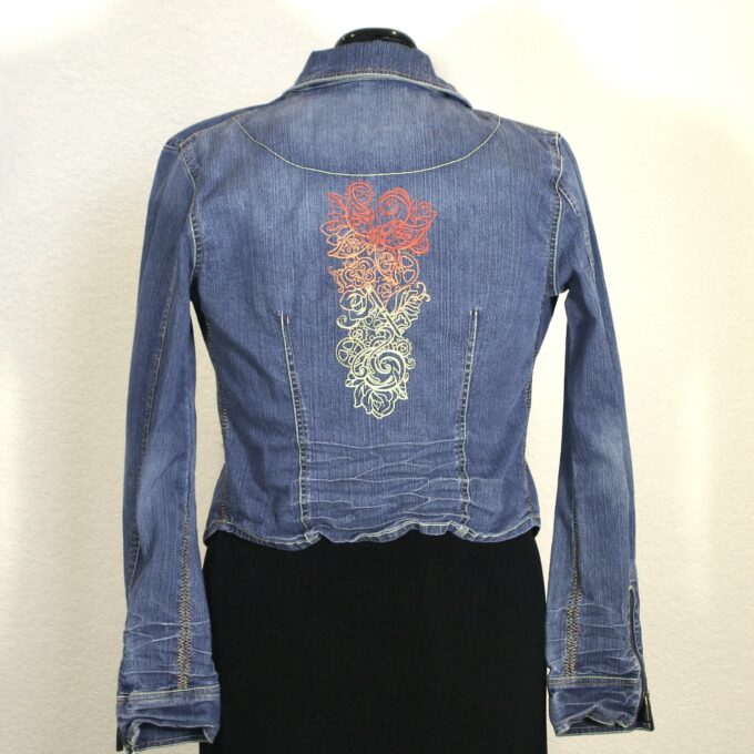 A denim jacket with an embroidered flower on it.