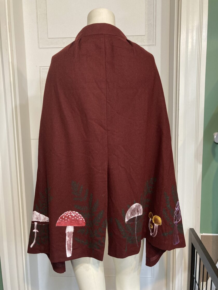 A mannequin displaying a burgundy cape with mushrooms on it.