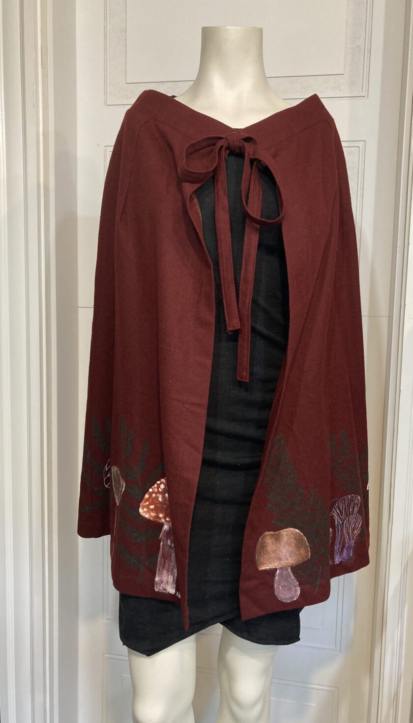 A mannequin mannequin wearing a burgundy cape with mushrooms on it.