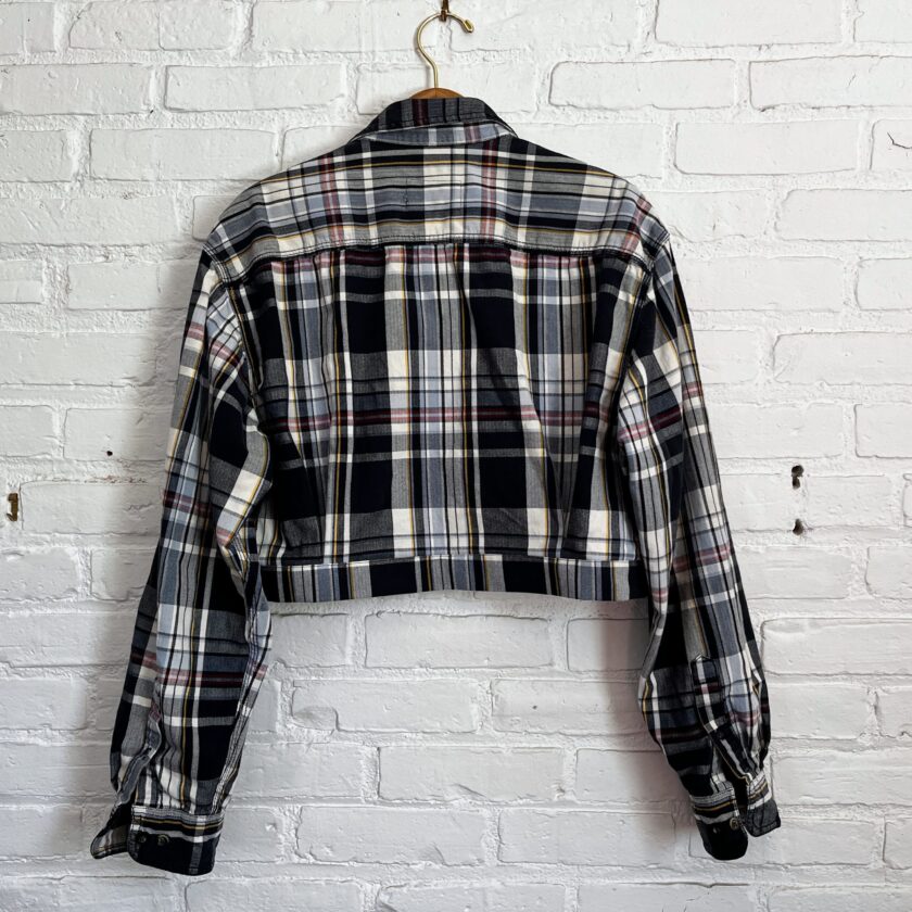 A black and white plaid jacket hanging on a brick wall.