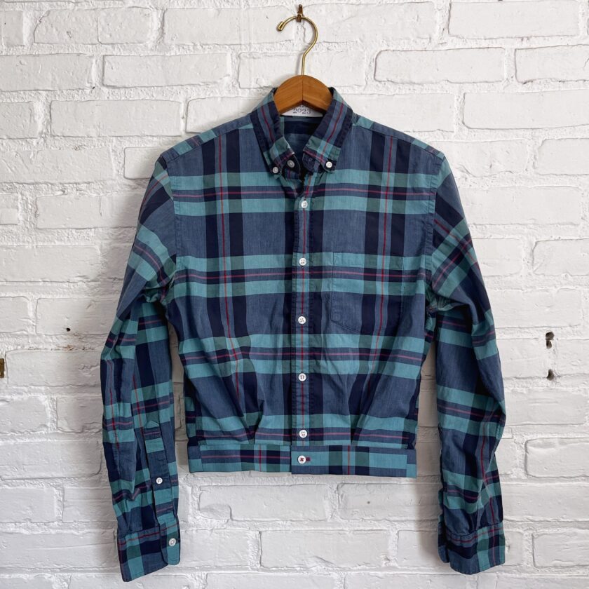 A blue and green plaid shirt hanging on a brick wall.