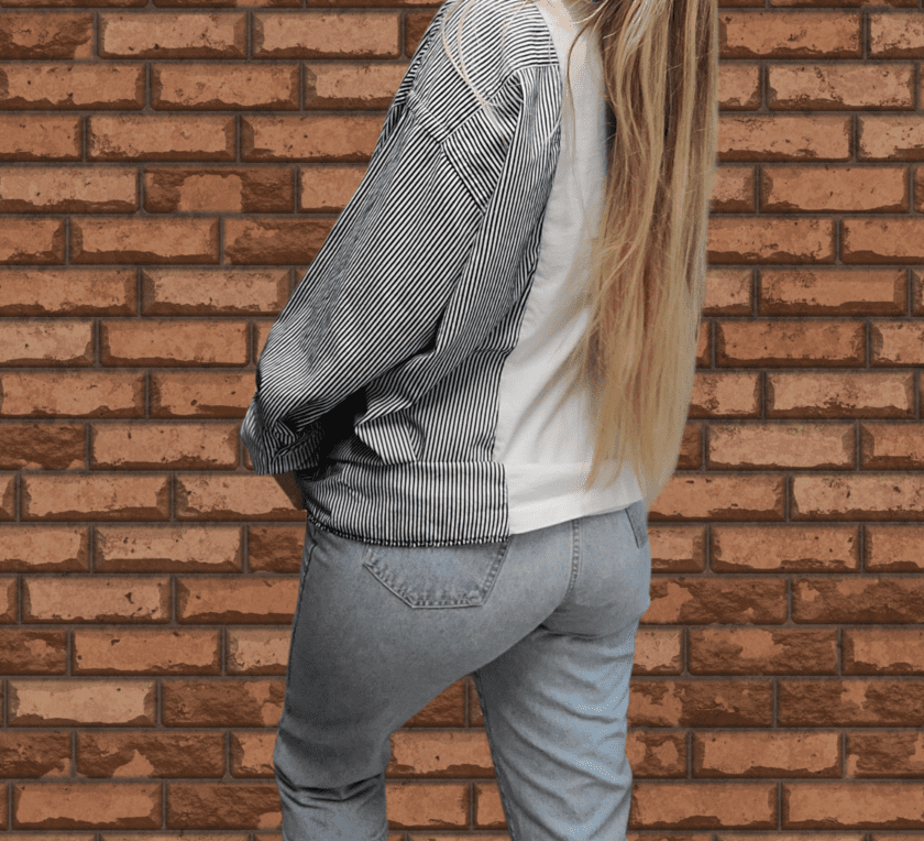 A woman wearing jeans and a jacket standing in front of a brick wall.
