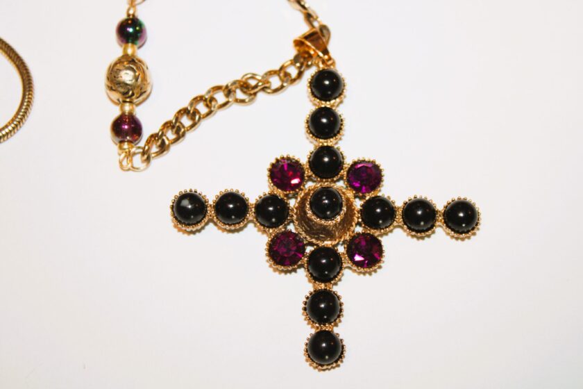 A gold cross necklace with black and purple stones.