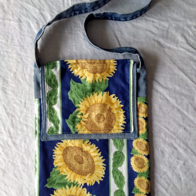 An upcycled denim messenger bag with sunflowers on it.