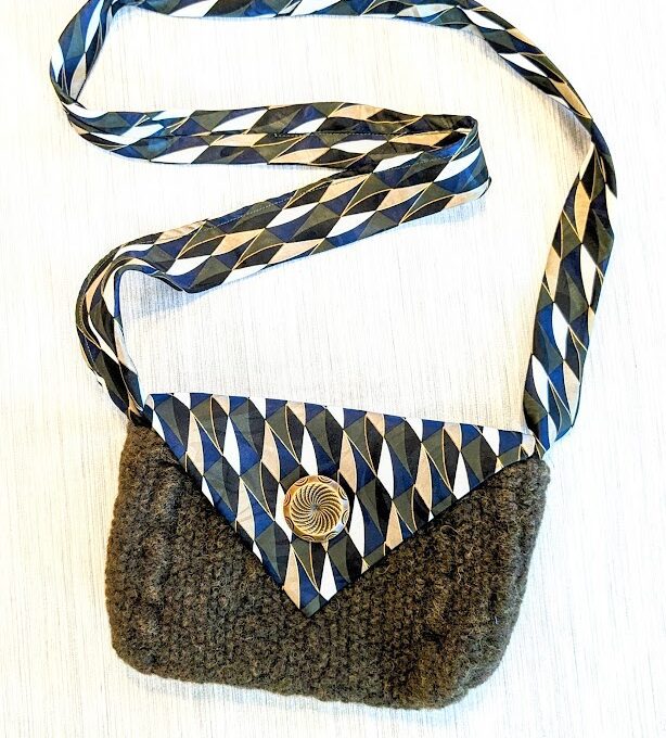 A knitted purse with a blue and white striped strap.