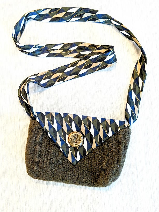 A knitted purse with a blue and white striped strap.