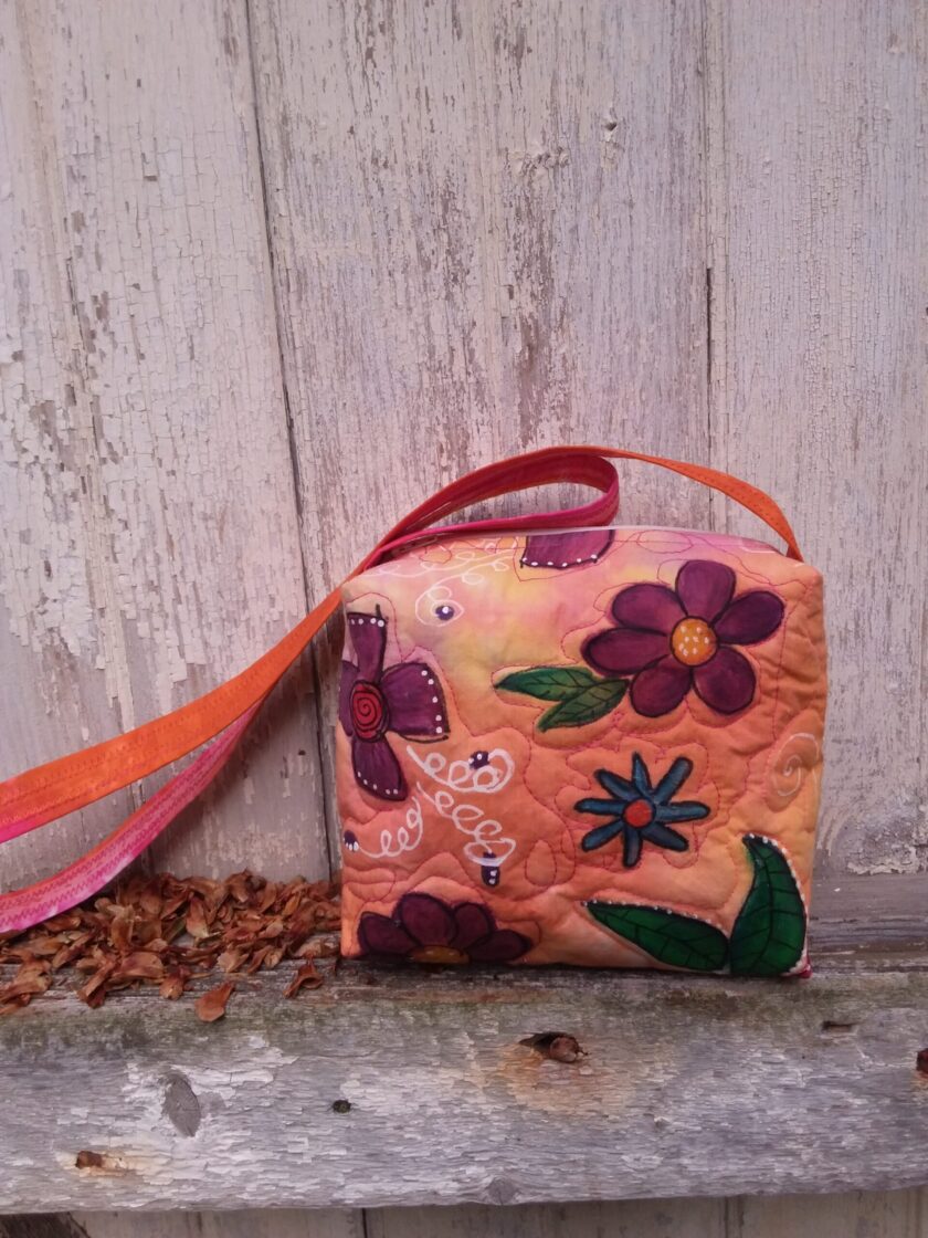 A unique, upcycled hand bag with painted flowers sitting on a shelf