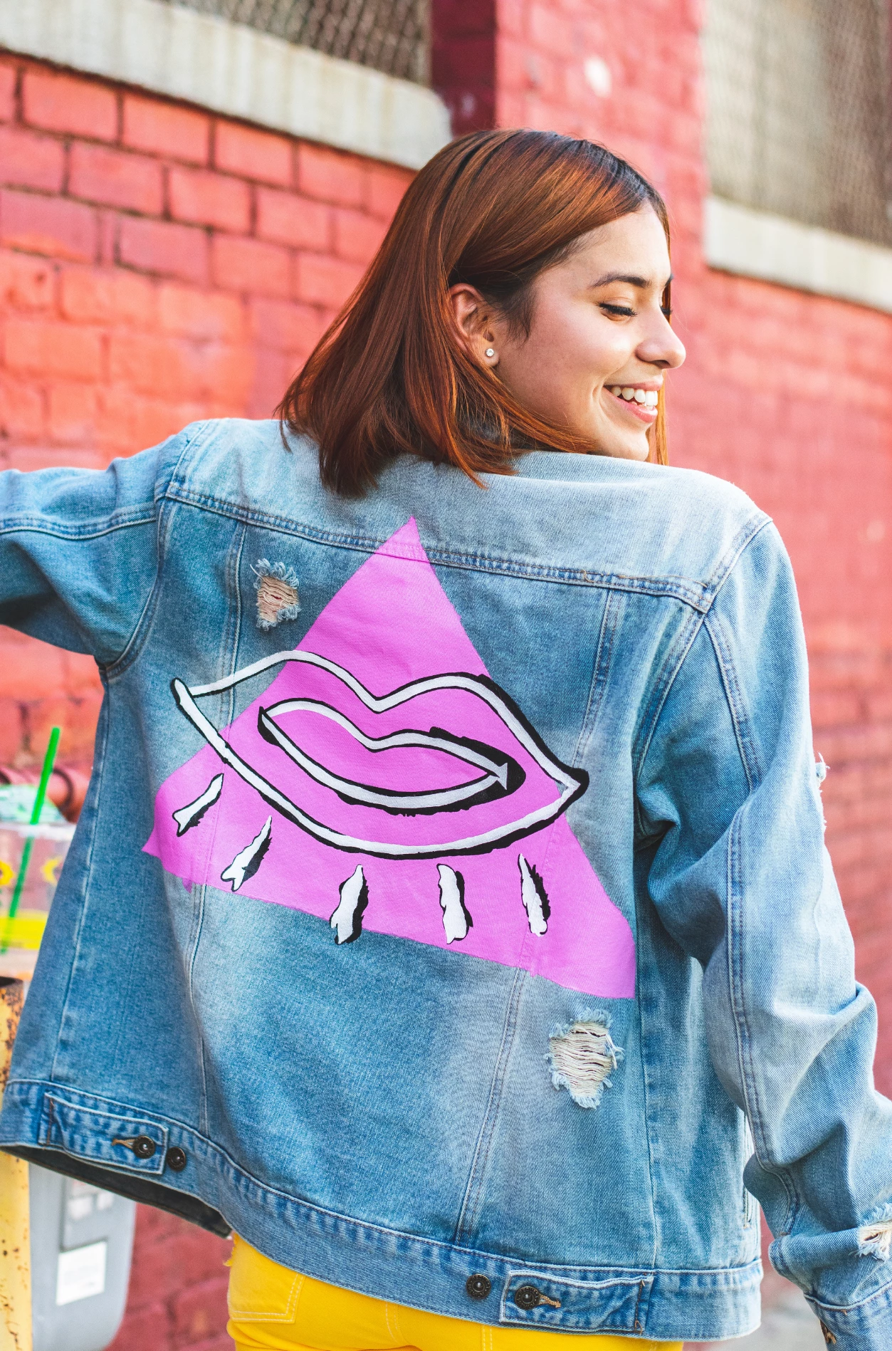 a woman wearing a denim jacket with a pink lips on it.